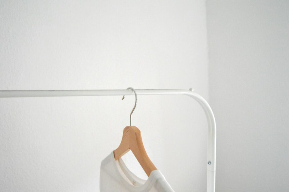 Illustrated capsule wardrobe for women with neutral mix-and-match tops, trousers, dresses, layers, shoes, and a tote on a rail